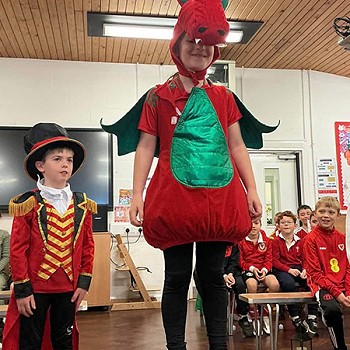 A child standing on a chair dressed up as a Welsh dragon