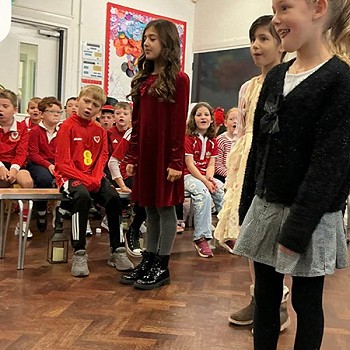 Three girls taking part in the year 3 and 4 assembly with children in the background