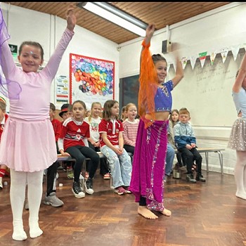 Three girls wearing colourful outfits and are dancing in the assembly